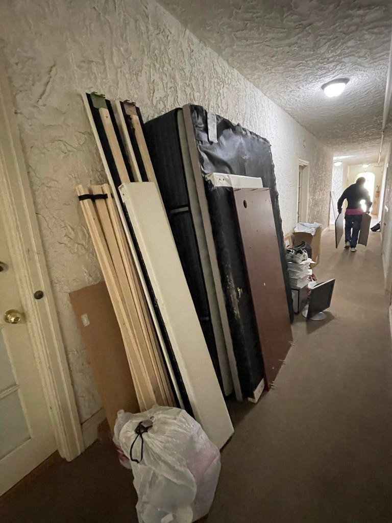 Disassembled bed frames and a mattress lean against a wall in a hallway in Hayward, California, suggesting junk removal in progress.