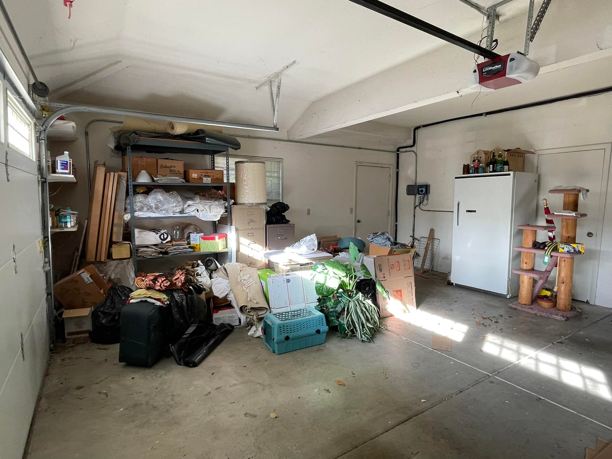 A cluttered garage filled with various household items, including shelving units with boxes, a white refrigerator, and miscellaneous junk.