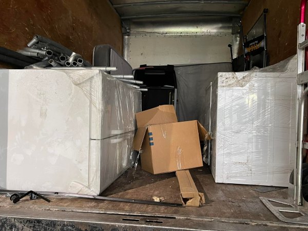 The inside of a moving truck in Hayward, California, packed with a wrapped refrigerator, metal pipes, cardboard boxes, and other household items.
