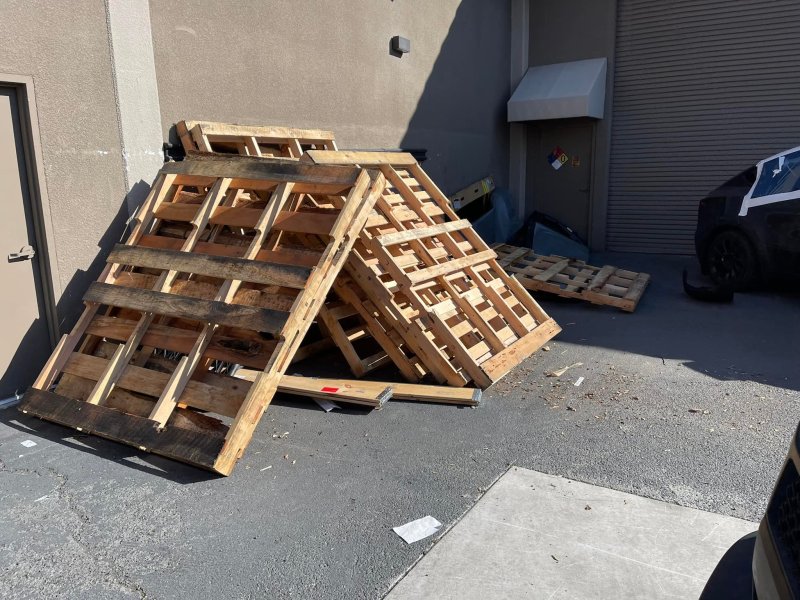A pile of discarded wooden pallets is leaning against a building on a paved surface, awaiting junk removal in Hayward, California.