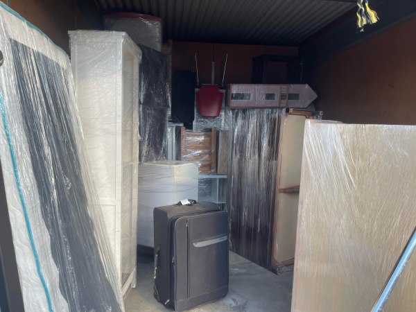 A cluttered storage unit filled with furniture and belongings wrapped in plastic.