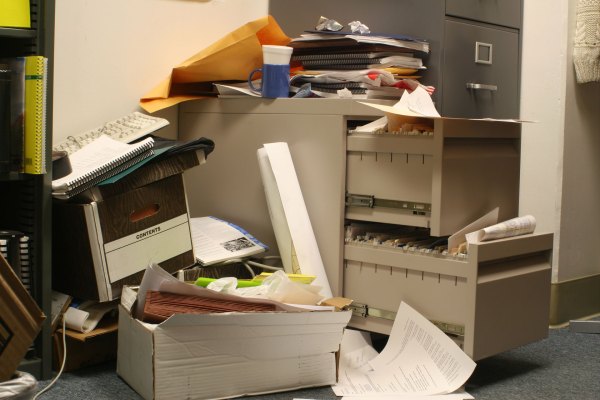 A cluttered office corner in Hayward, California, with an overflowing file cabinet, stacks of papers, and boxes piled around it.
