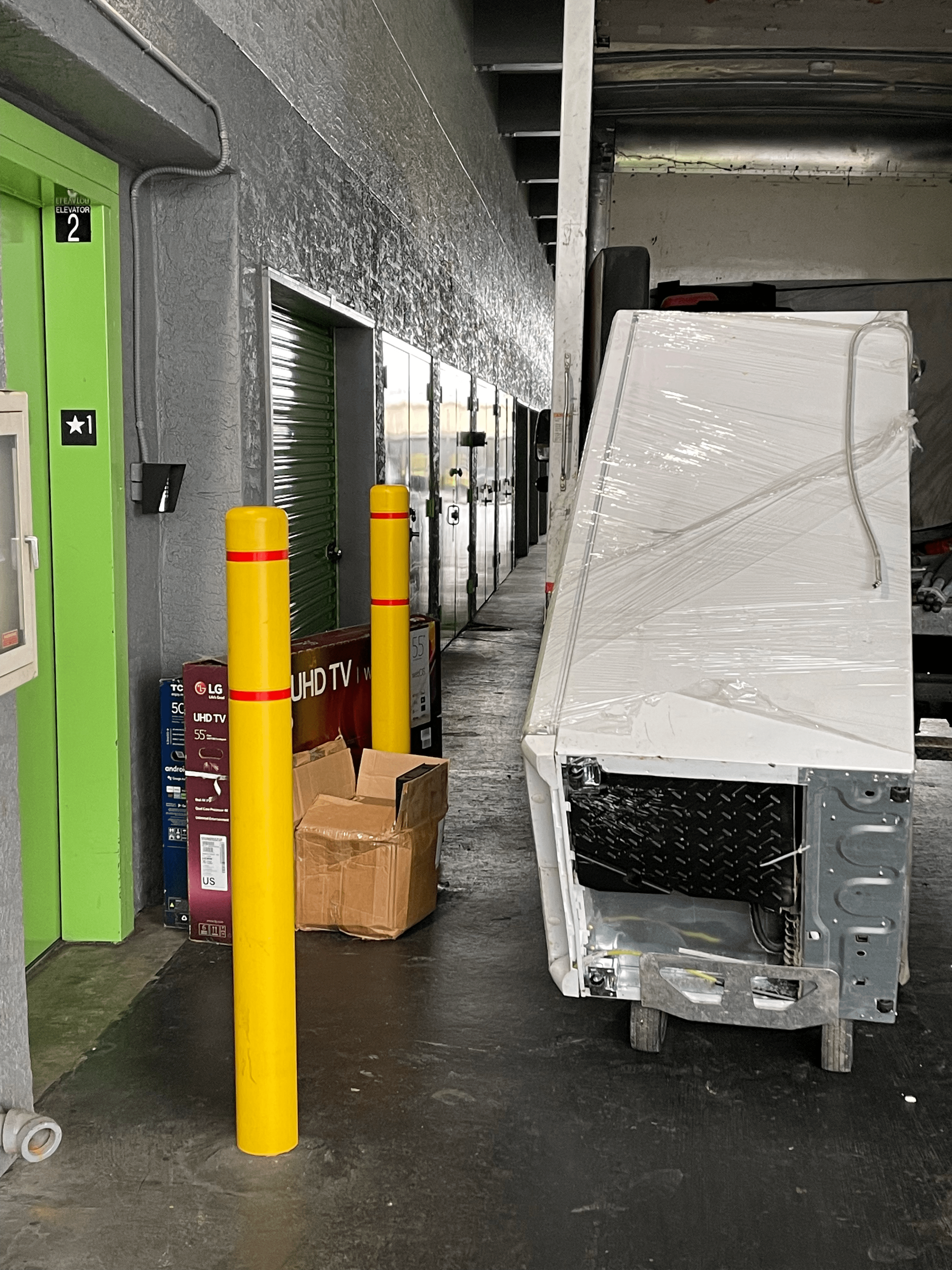A wrapped refrigerator is being discarded in a storage unit facility hallway near closed unit doors and discarded box