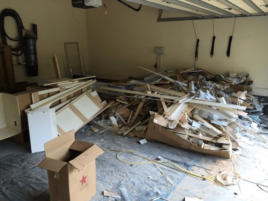 A cluttered garage in Hayward CA, filled with construction debris like wood scraps, cardboard boxes, and other discarded materials awaiting junk removal.